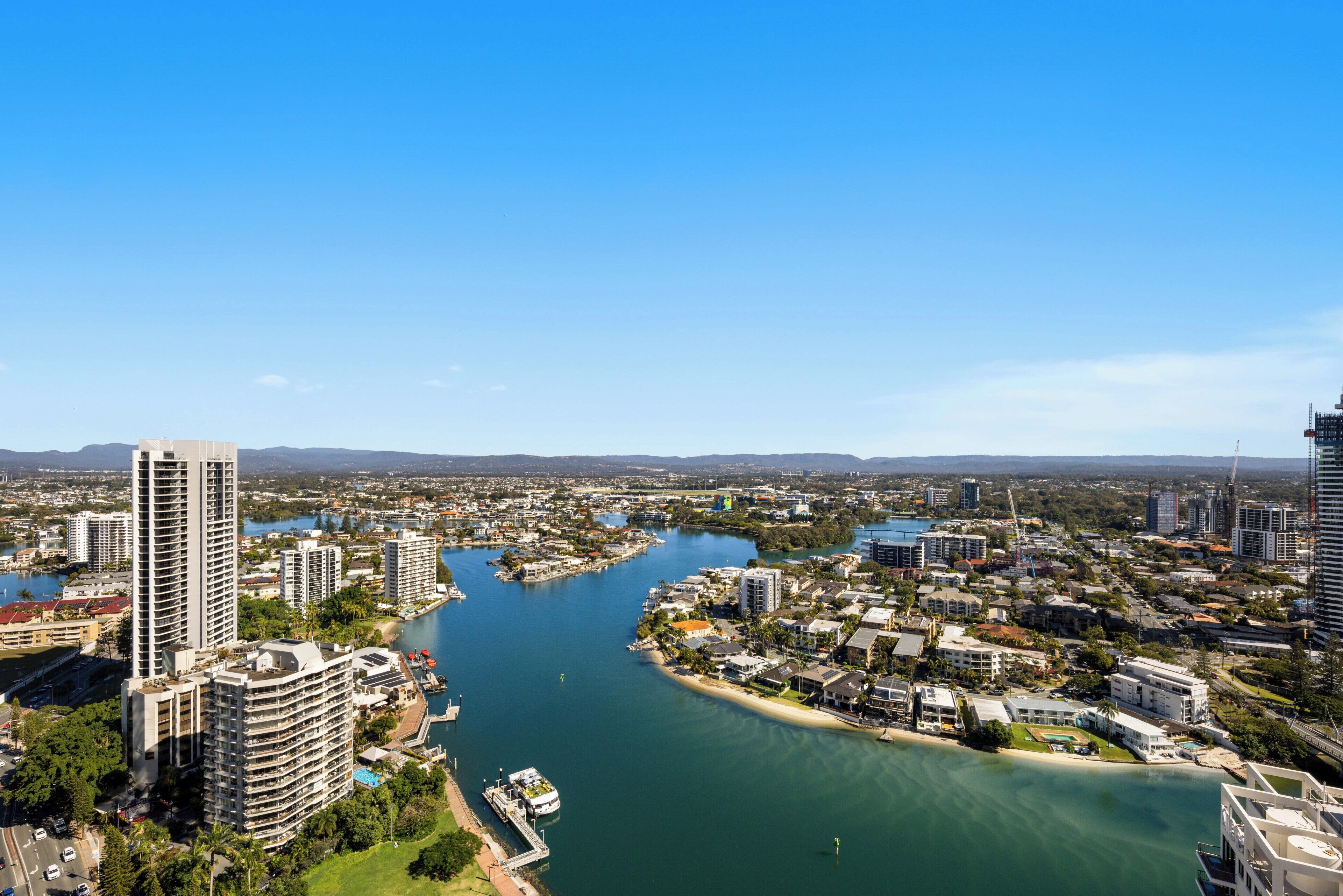 A coastal cityscape with high-rise buildings, a marina, and a river.