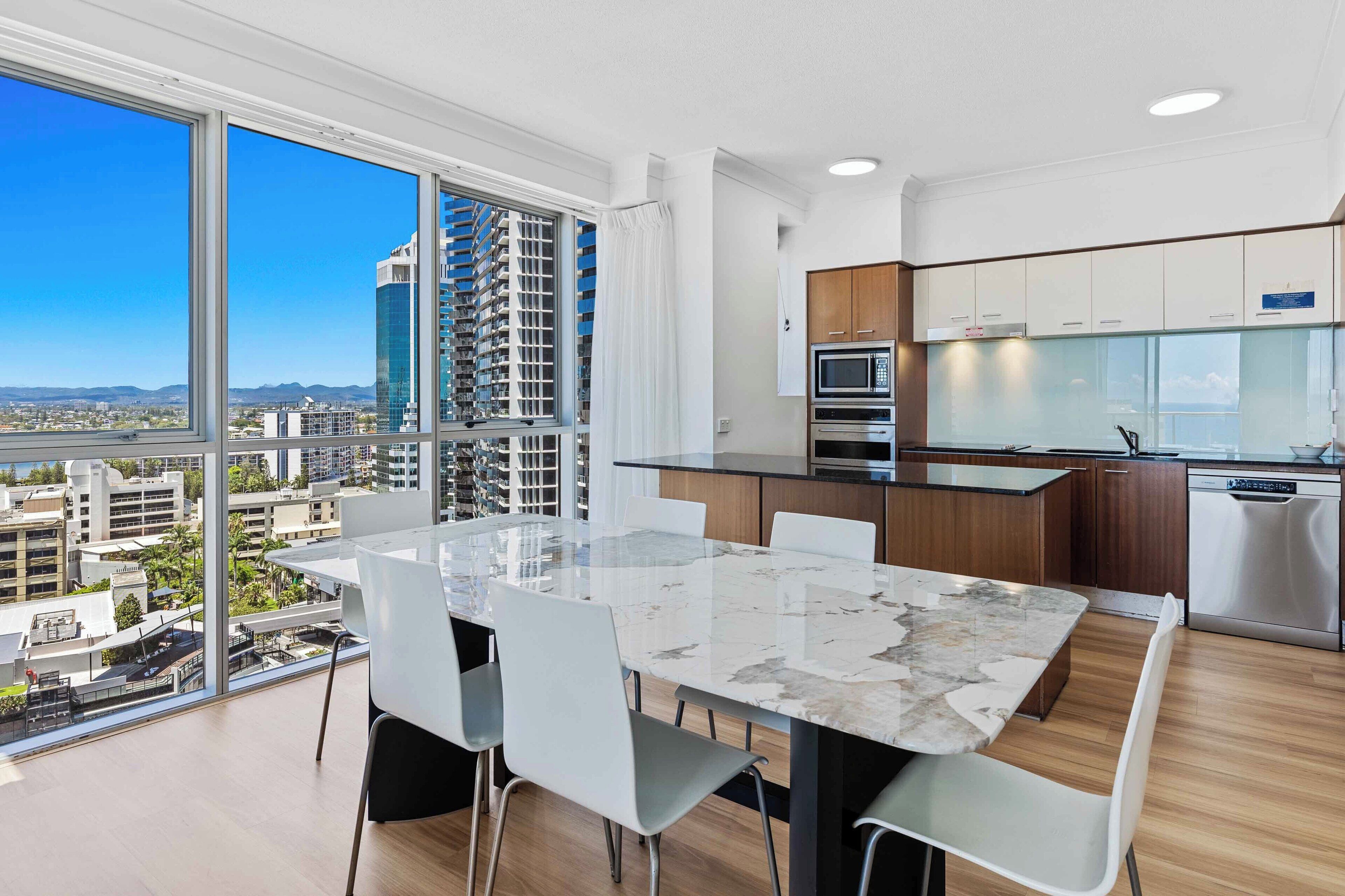A modern kitchen with a large island, white cabinetry, and a view of a cityscape through large windows.