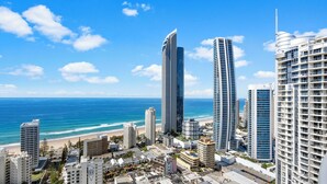A coastal cityscape with modern high-rise buildings, a beach, and a clear blue sky.