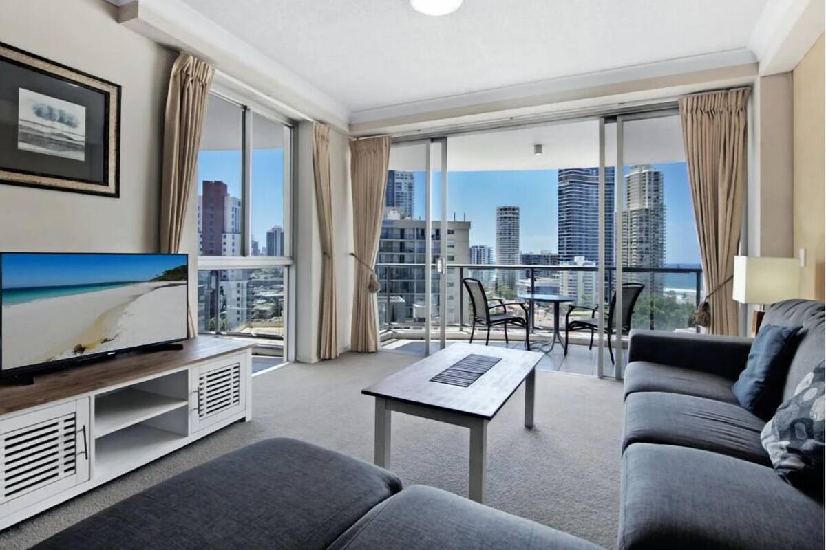 Ett modernt hotellrum med en balkong, en platt-TV, en soffa, ett soffbord och utsikt över staden.