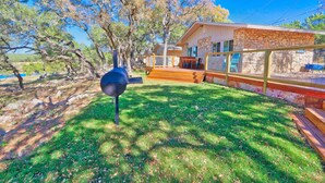 Un jardin avec un barbecue, une maison en pierre dotée d’une terrasse et un espace clos avec des chaises.