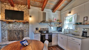 Une cuisine dotée d’une cheminée en pierre, d’un four encastré, de meubles blancs et d’un coin repas avec une table et des chaises en bois.