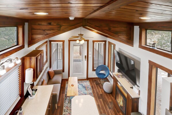 A cozy interior with a wooden ceiling, a ceiling fan, a large TV, and a seating area with a sofa and a coffee table.