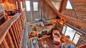 A cozy log cabin interior with a stone fireplace, wooden furniture, and a ceiling fan. - Log Cabin at Old Glory Ranch | Take a trip back in time! (Wimberley)