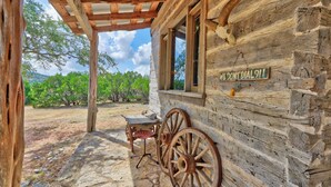 A rustic log cabin with a covered porch, a wooden table, and a sign that reads "WE DON'T DIAL 91!". - Log Cabin at Old Glory Ranch | Take a trip back in time! (Wimberley)