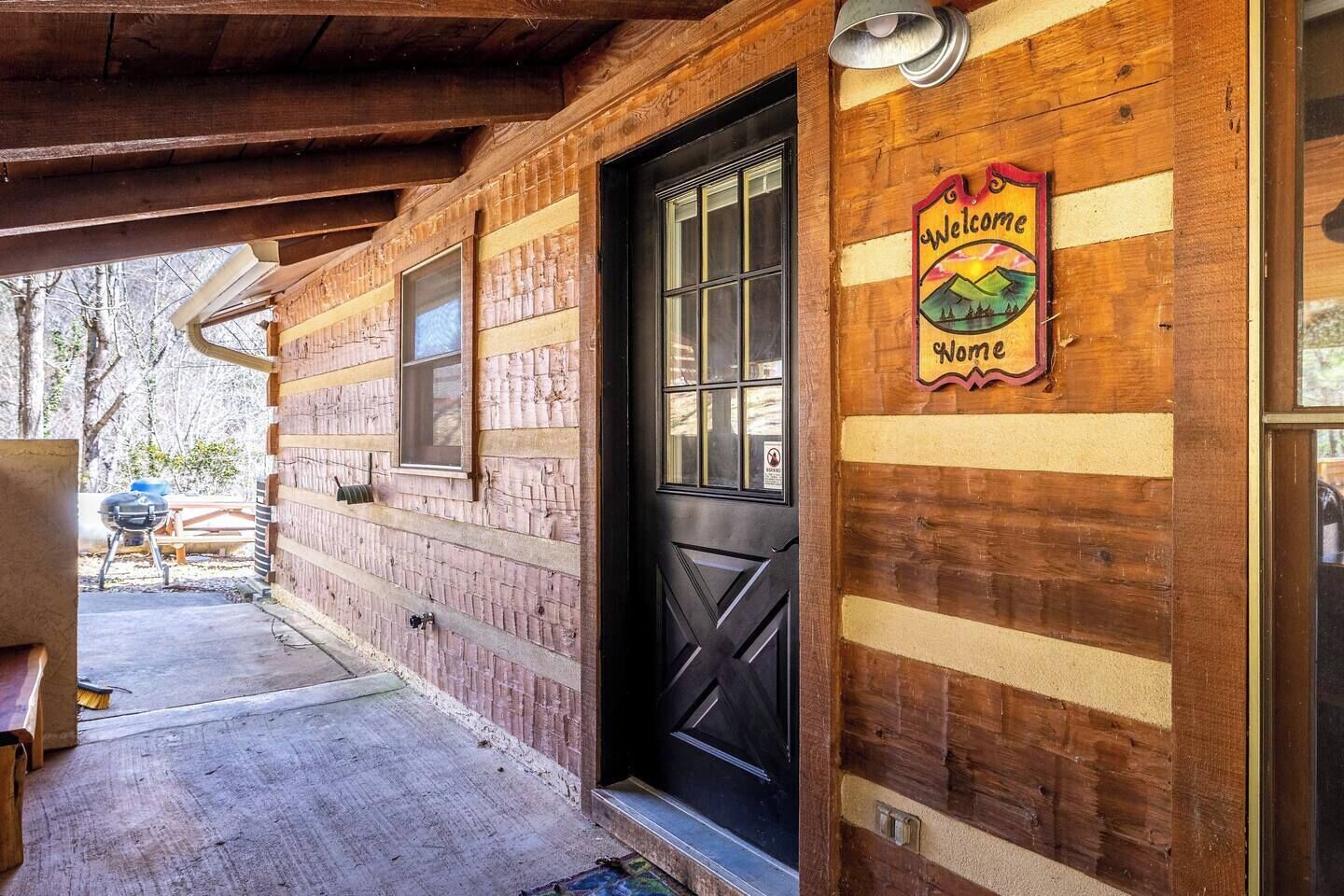 Una cabaña de madera con puerta negra y un letrero de bienvenida.