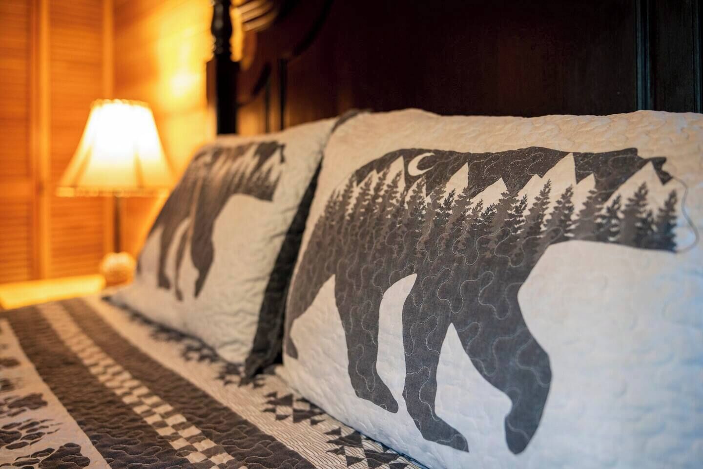 A bed with two pillows featuring a bear design, a patterned blanket, and a lamp in the background.