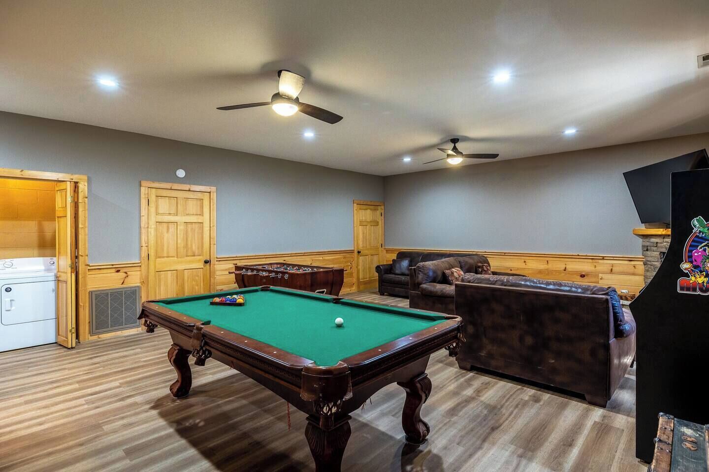 Una mesa de billar en una habitación con ventilador de techo, sofá y chimenea.