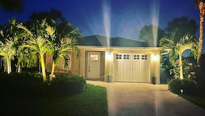 A two-story house with a garage, surrounded by palm trees and a well-maintained lawn. - Luxury Beach House • Pool & Hot Tub Oasis (Naples)