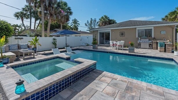 A swimming pool with a tiled deck, a patio area with outdoor furniture, and a house with a covered patio and barbecue area. - Luxury Beach House • Pool & Hot Tub Oasis (Naples)