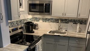 Una cocina moderna con armarios blancos, un refrigerador de acero inoxidable, un microondas, una estufa y un lavamanos.