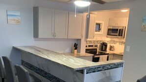 Una cocina con una isla central, taburetes de bar, un ventilador de techo y un microondas.