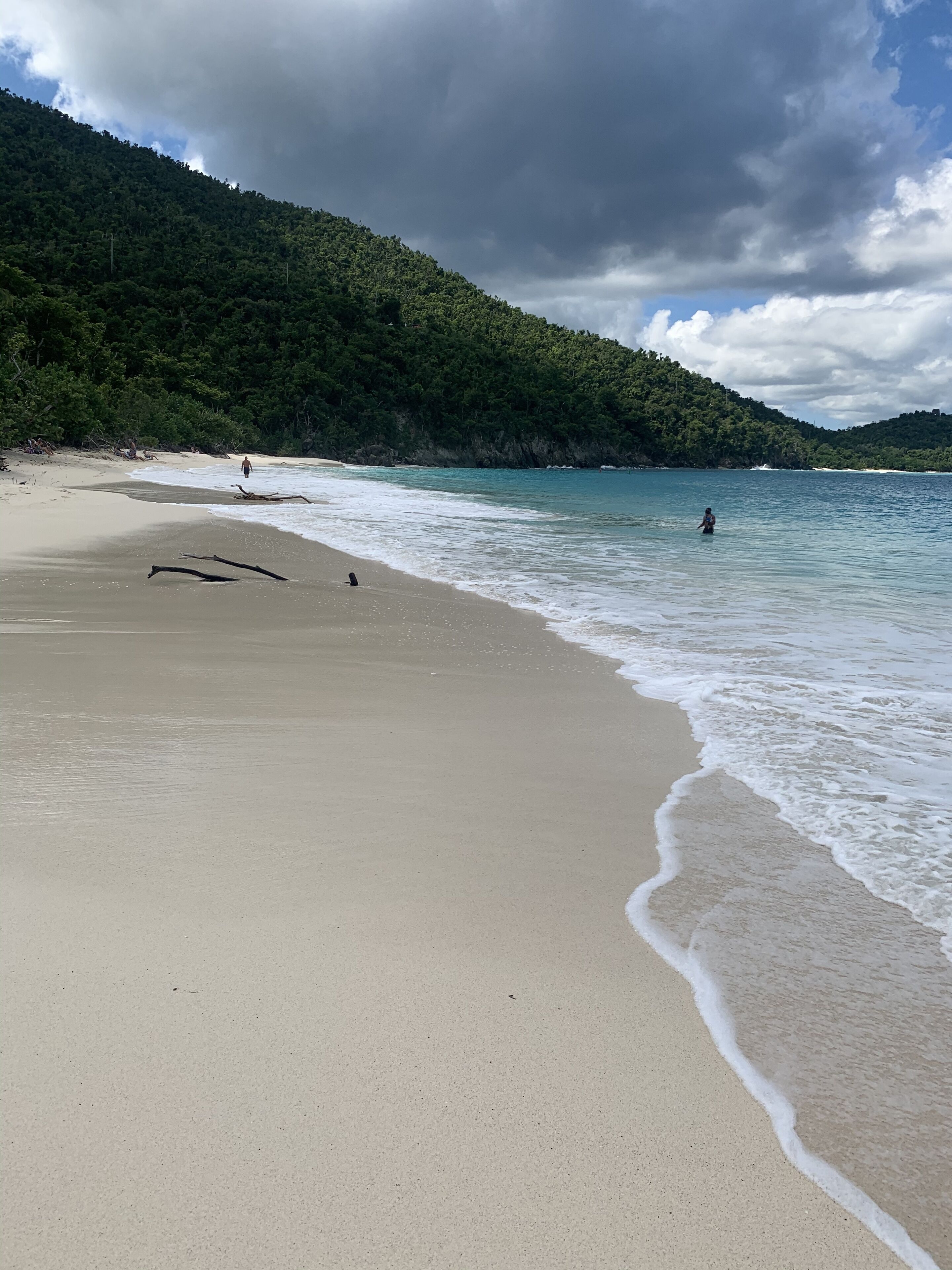Una playa con agua cristalina, una orilla de arena y una colina boscosa al fondo.