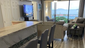Una cocina moderna con encimera de mármol, taburetes para bar y televisor.