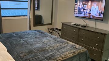Een slaapkamer met een bed, een aan de muur bevestigde televisie, een plafondventilator en een raam met uitzicht op de oceaan.