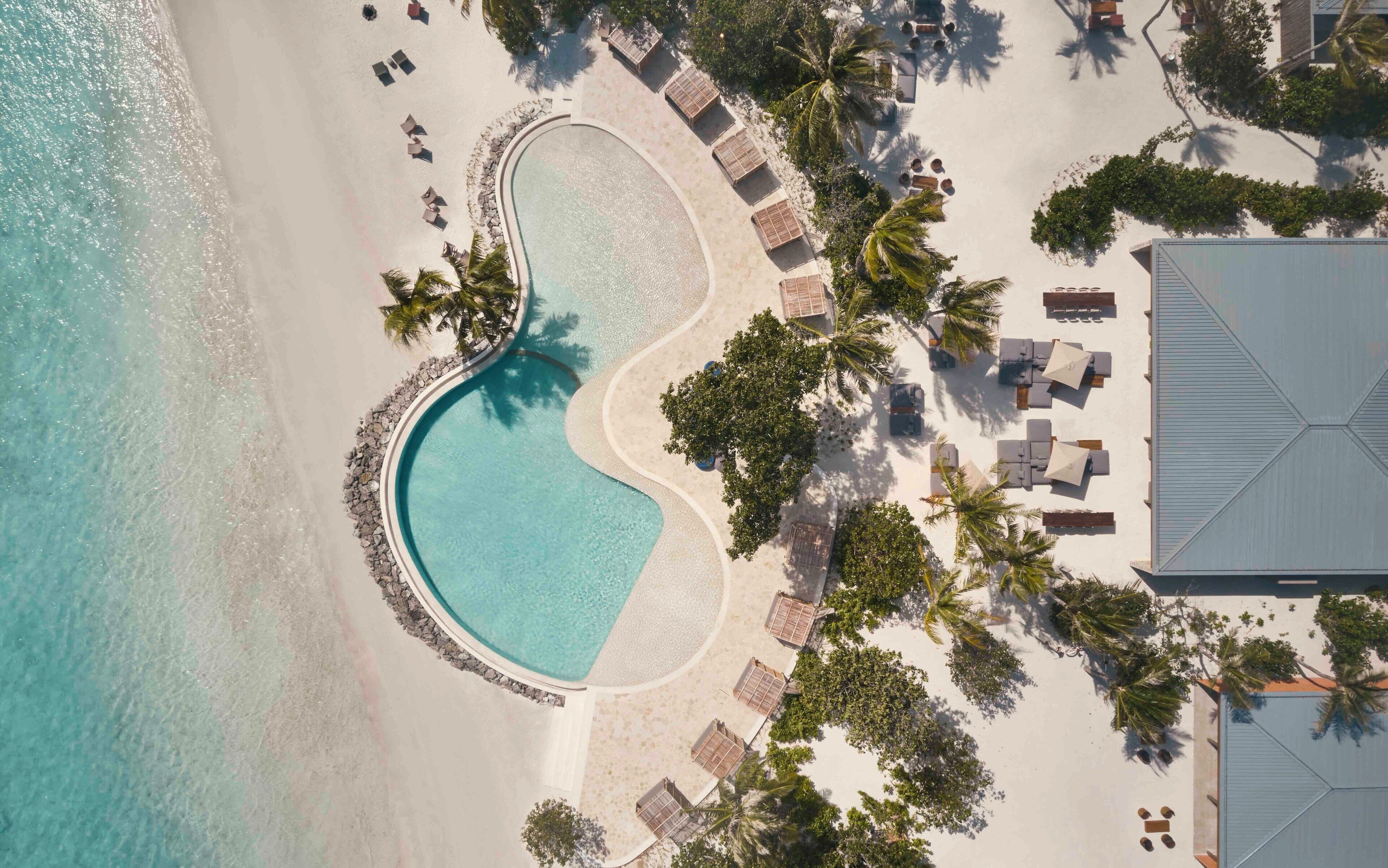 Vista aérea de un resort con piscina central, tumbonas y palmeras.