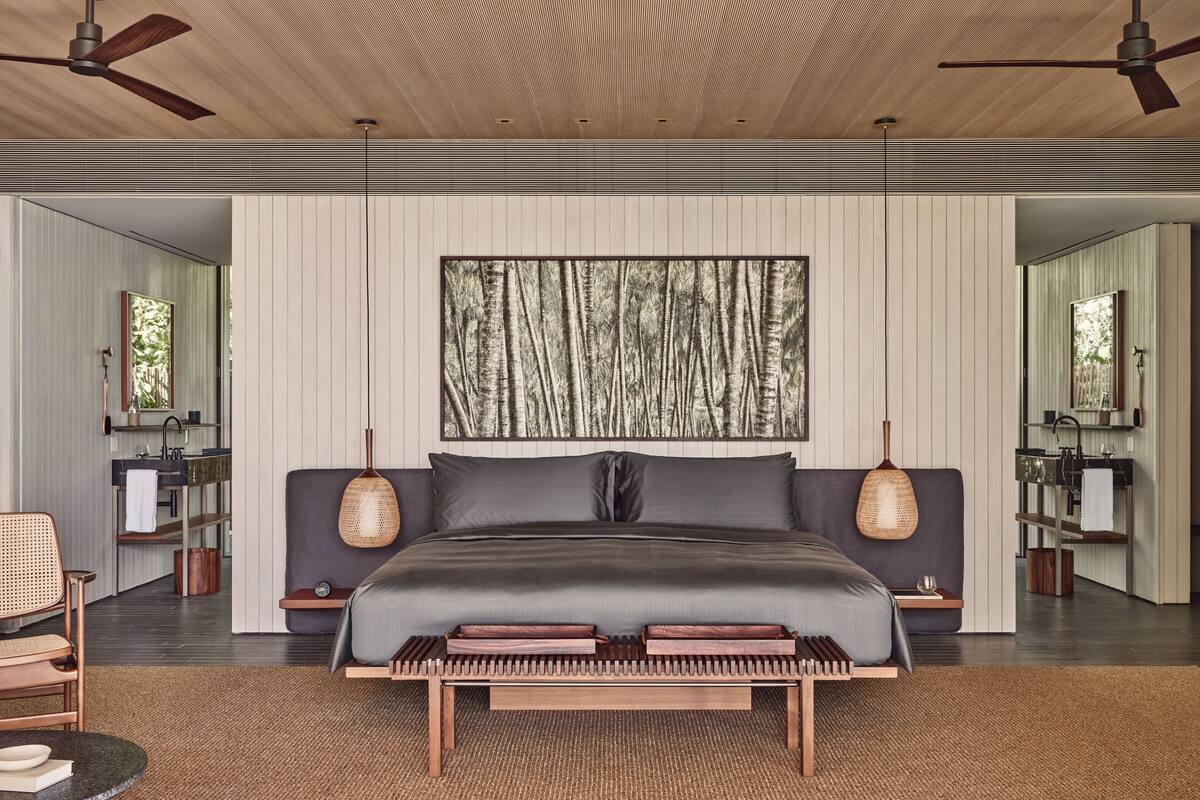 Une chambre à coucher moderne avec un grand lit, deux tables de chevet, une œuvre d’art accrochée au mur et un ventilateur de plafond.