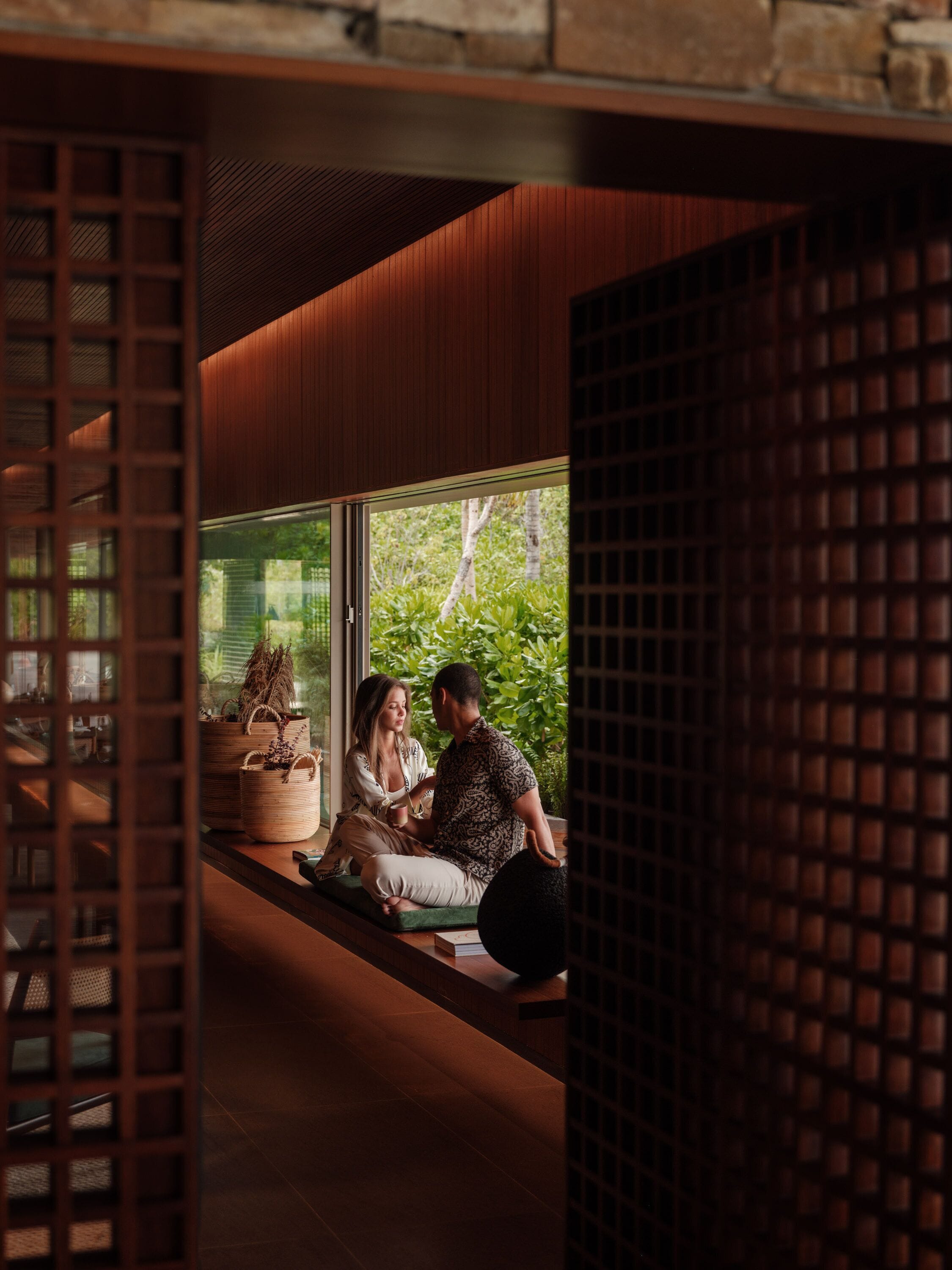 Interior moderno com um banco de madeira, plantas em vasos e vista para o verde lá fora.