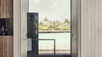 Un baño moderno con ducha, lavamanos y vistas a una playa tropical.