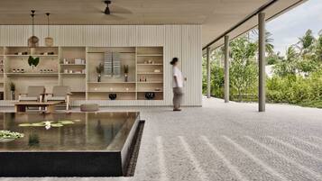 A modern interior with a large open space, a seating area with a water feature, and a view of lush greenery outside.