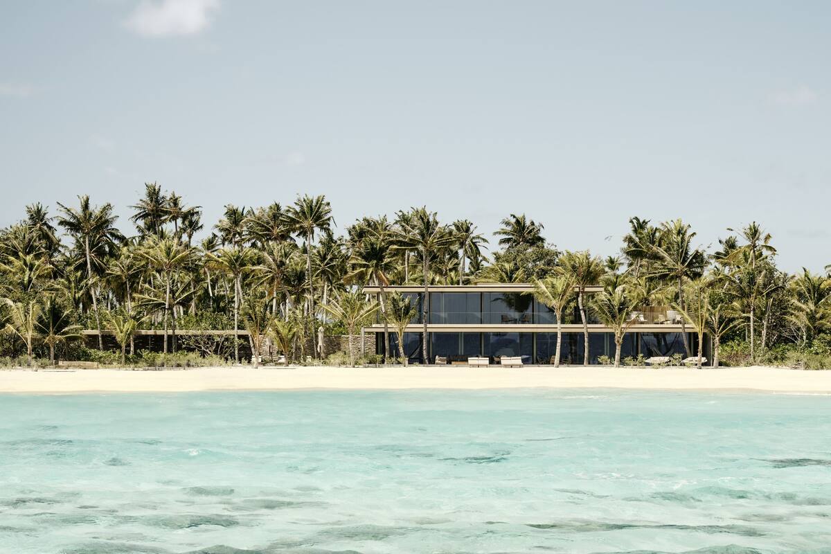 Une propriété située en bord de mer, avec un bâtiment moderne à deux étages, une plage de sable et des palmiers.