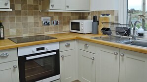A kitchen with a microwave, oven, and sink. There is a sign on the wall and a bottle of olive oil on the counter. - Kirklauchline Cottage (Stoneykirk, near Portpatrick)
