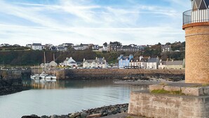 A coastal town with a lighthouse, stone walls, and a marina with boats. - Kirklauchline Cottage (Stoneykirk, near Portpatrick)