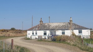 A white house with a dirt driveway, a parked car, and a wooden fence. - Kirklauchline Cottage (Stoneykirk, near Portpatrick)