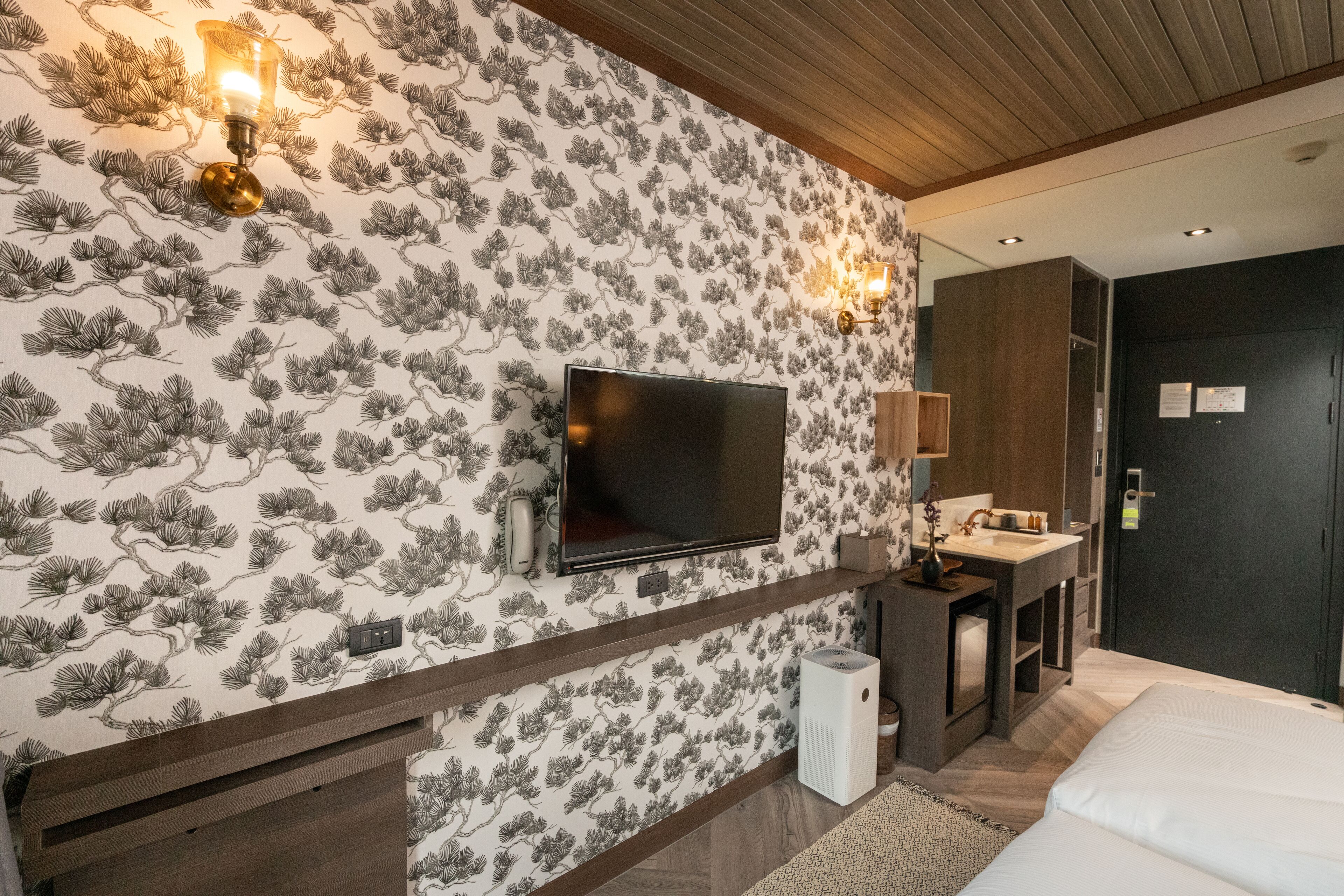 A bedroom with a TV mounted on the wall, a bedside table, a lamp, and a bed.