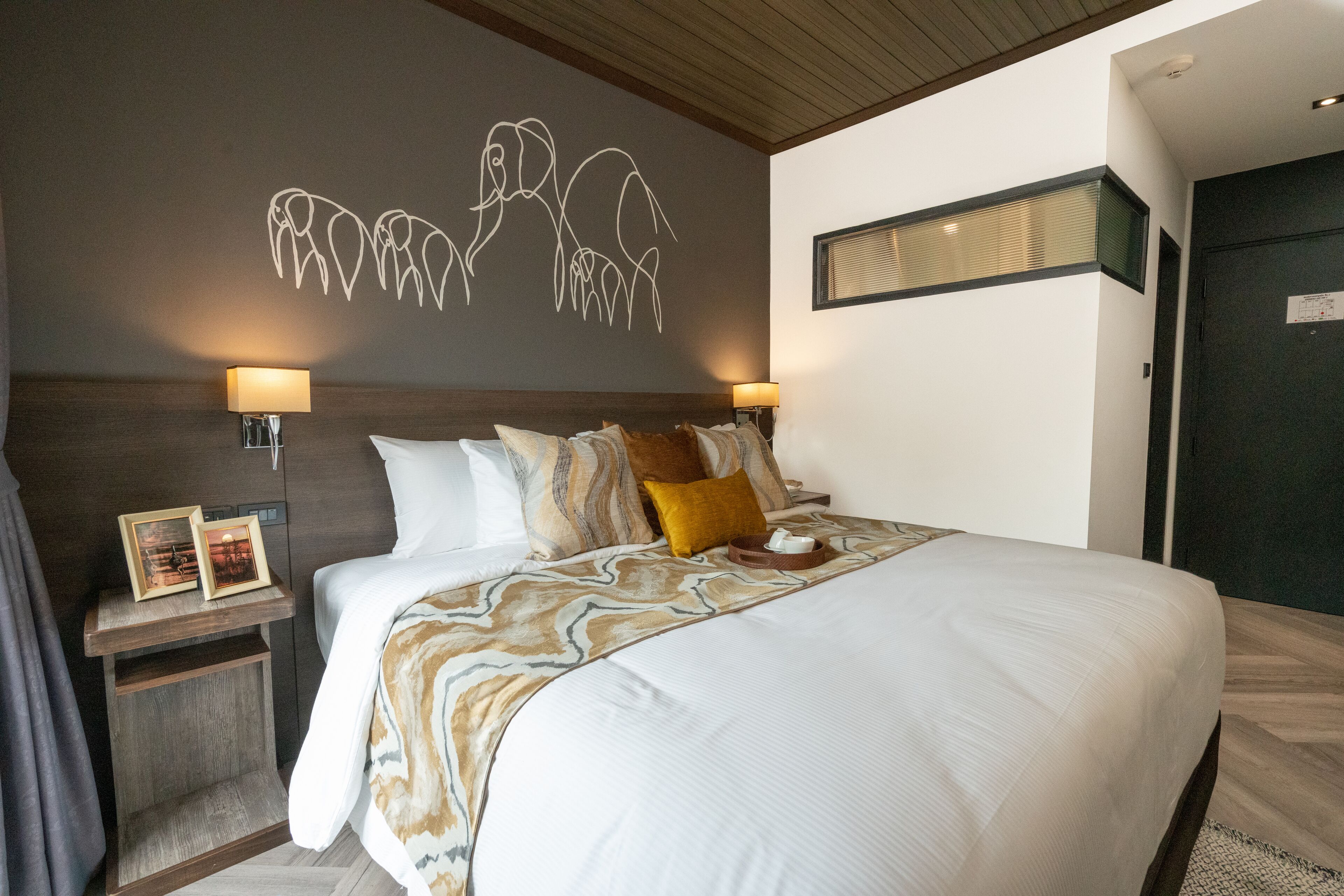 Cama bem arrumada com colcha estampada, duas luminárias de cabeceira e uma obra de arte na parede acima da cama.