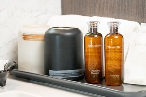 A bathroom vanity with a black and white soap dispenser, two bottles of shower gel, and a white towel.