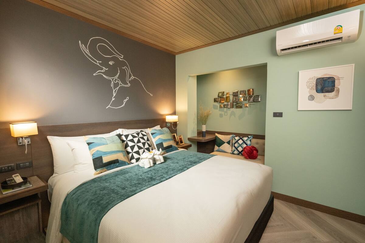 A hotel room with a bed, nightstands, a wall-mounted air conditioner, and a wall with framed pictures.