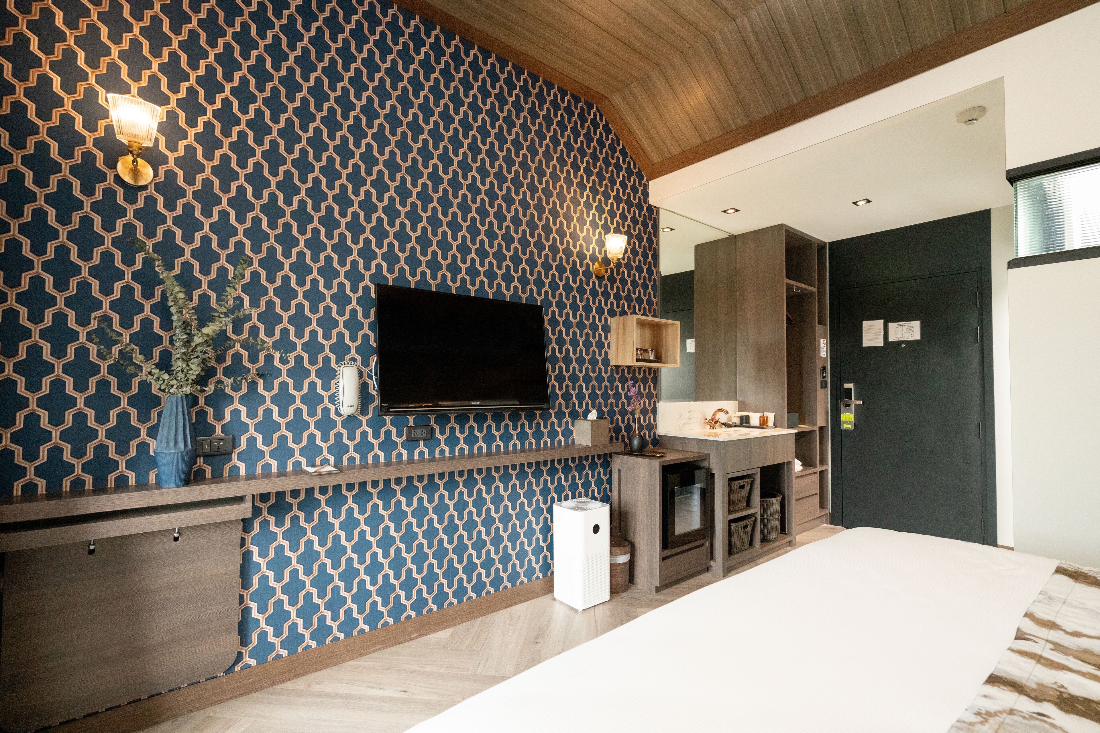 A modern room with a patterned wall, a flat-screen TV, built-in wooden cabinets, and a small white trash bin.