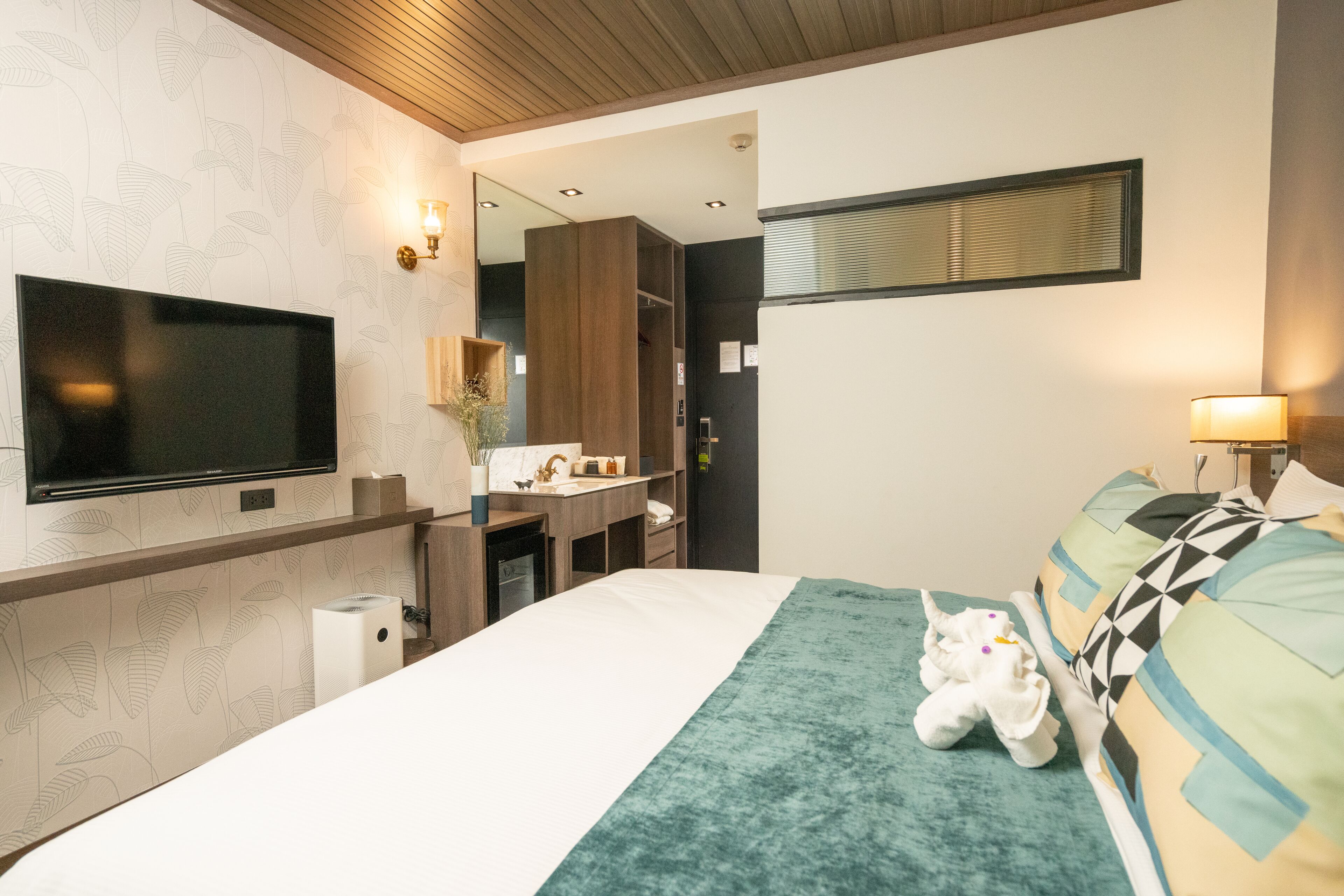 A modern hotel room with a large bed, a flat-screen TV, a mirror, and a bathroom area with a sink and mirror.