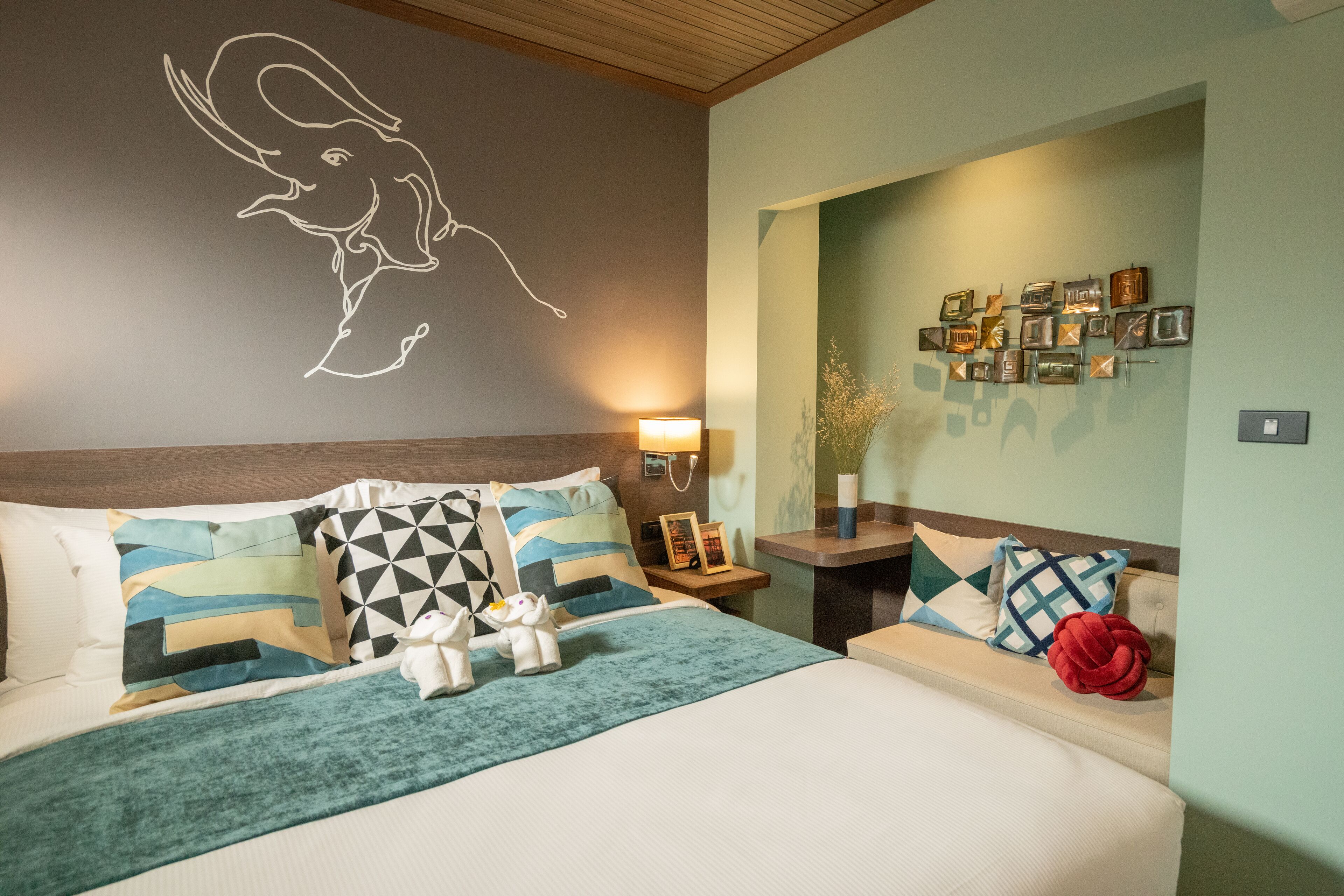 A hotel room with a bed, a nightstand, a wall with a decorative elephant outline, and a wall with framed pictures.
