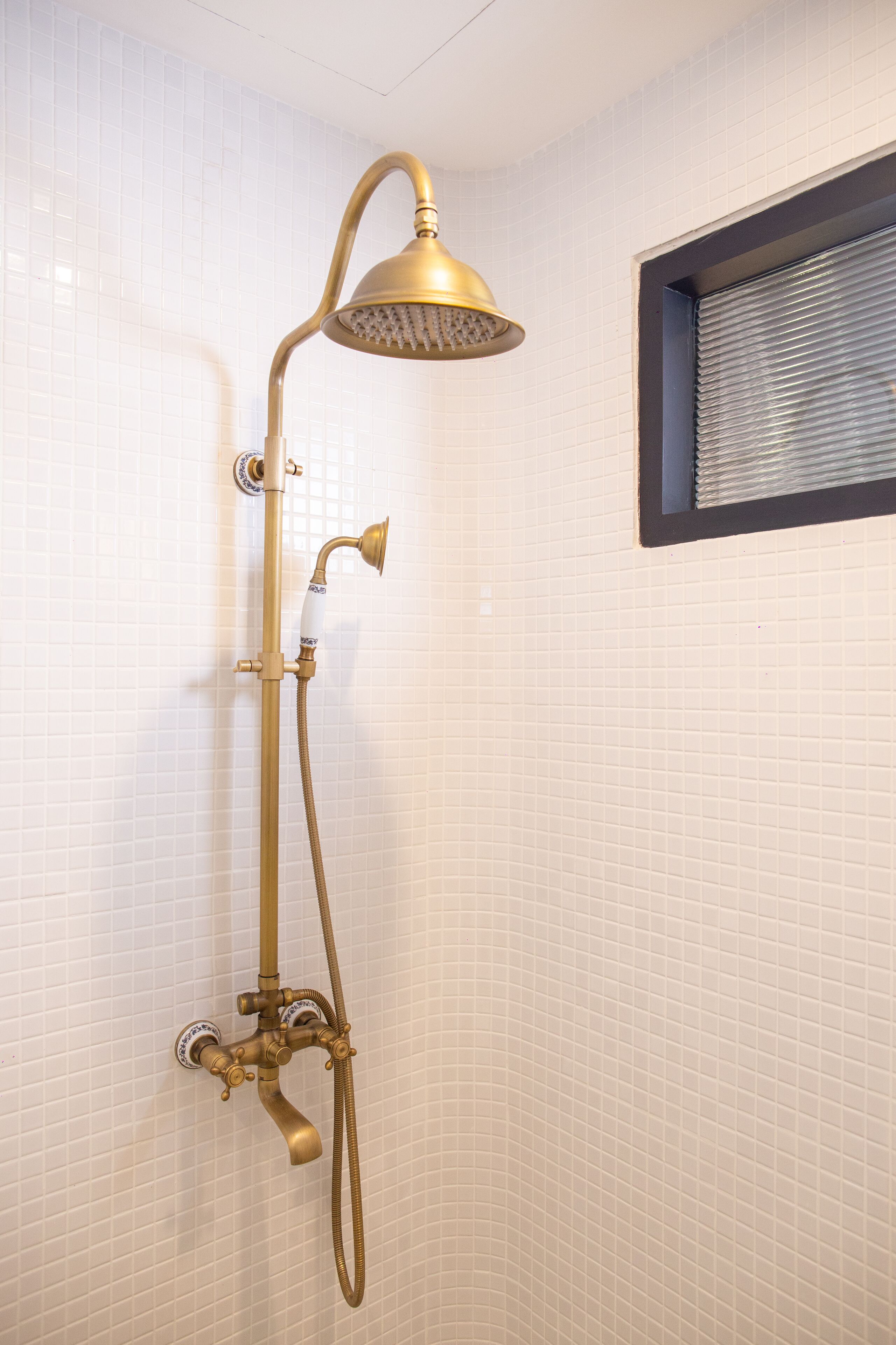 A shower with a gold-colored showerhead and hose, mounted on a tiled wall.