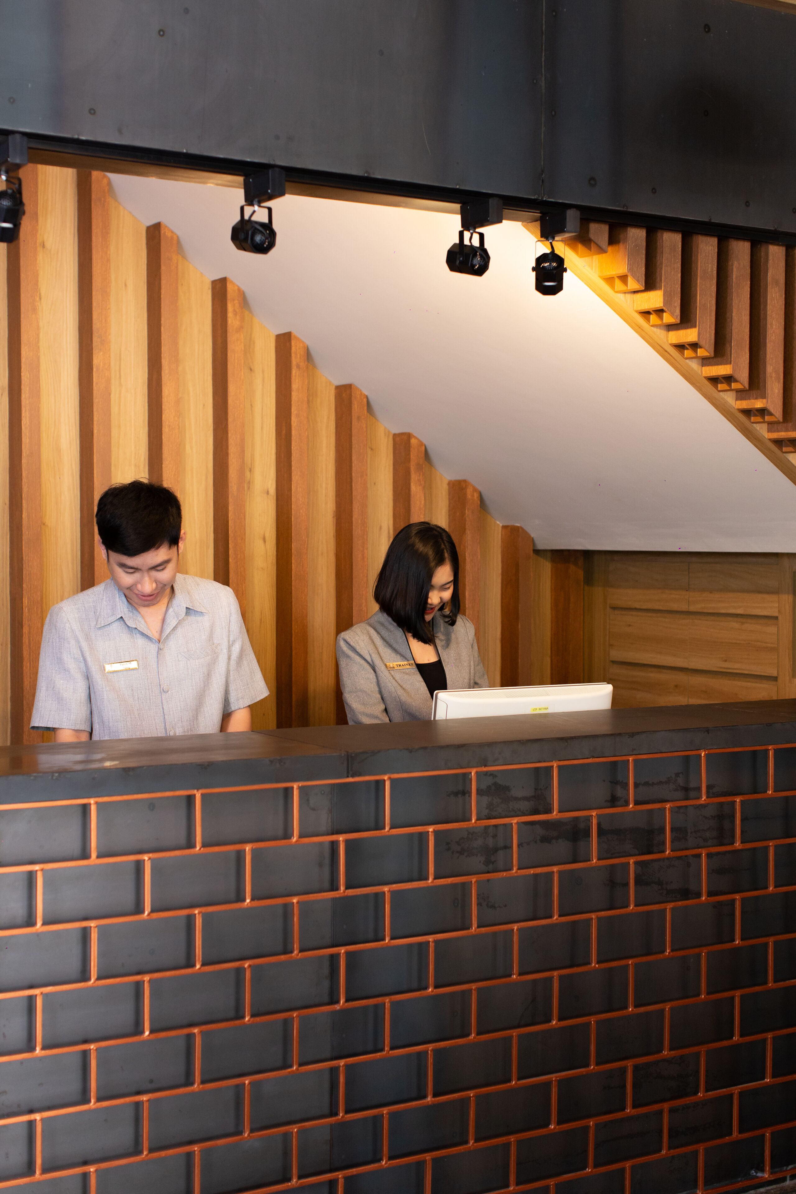 Un comptoir d’accueil avec un mur en panneaux de bois et, en dessous, un mur en briques noires.