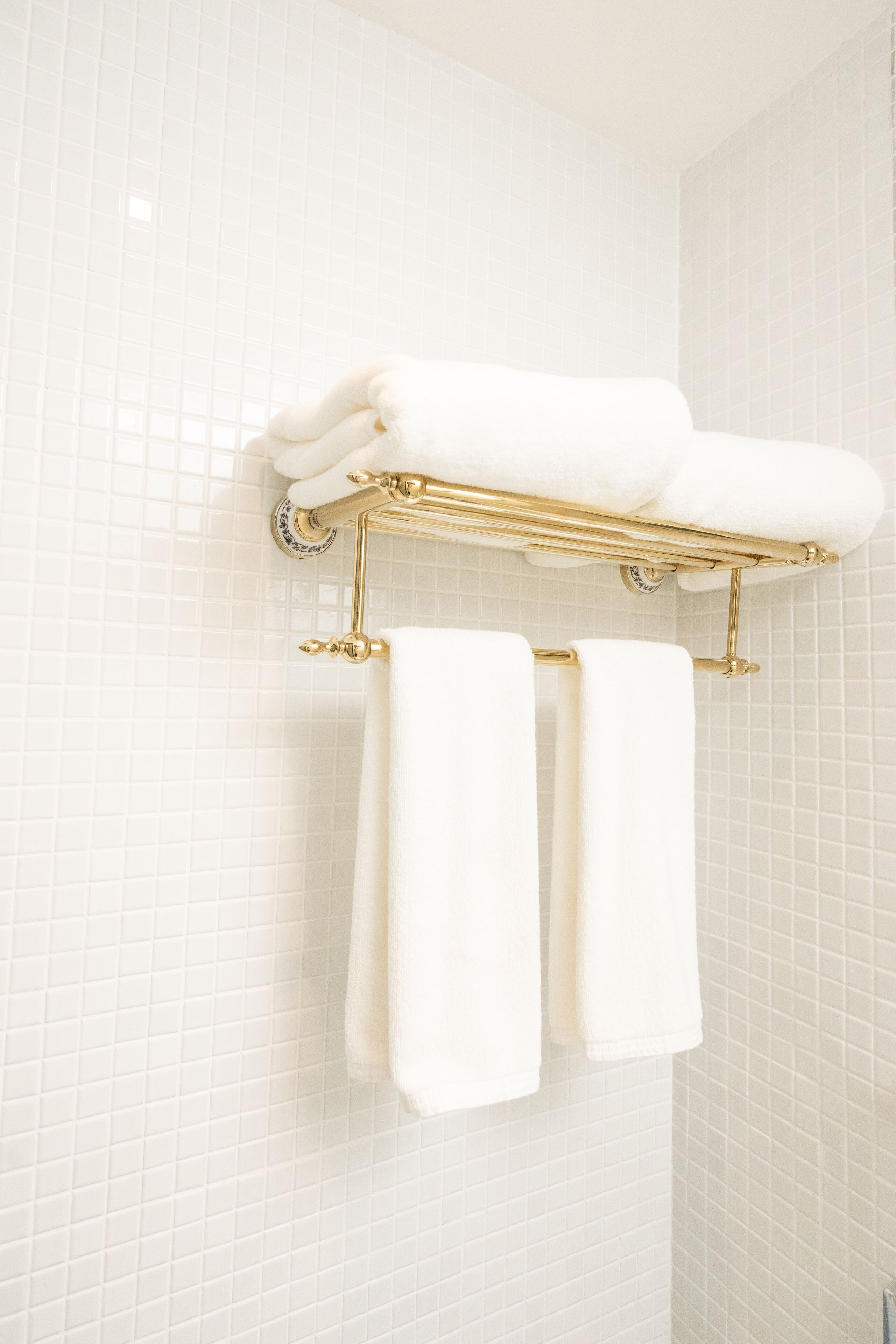 Un baño con paredes de azulejos blancos y un toallero dorado con tres toallas dobladas.