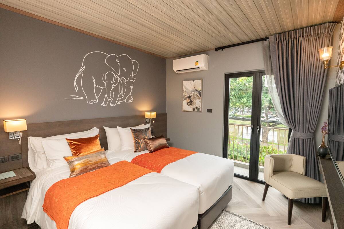 A hotel room with a large bed, two bedside tables, a chair, a balcony with curtains, and wall art.