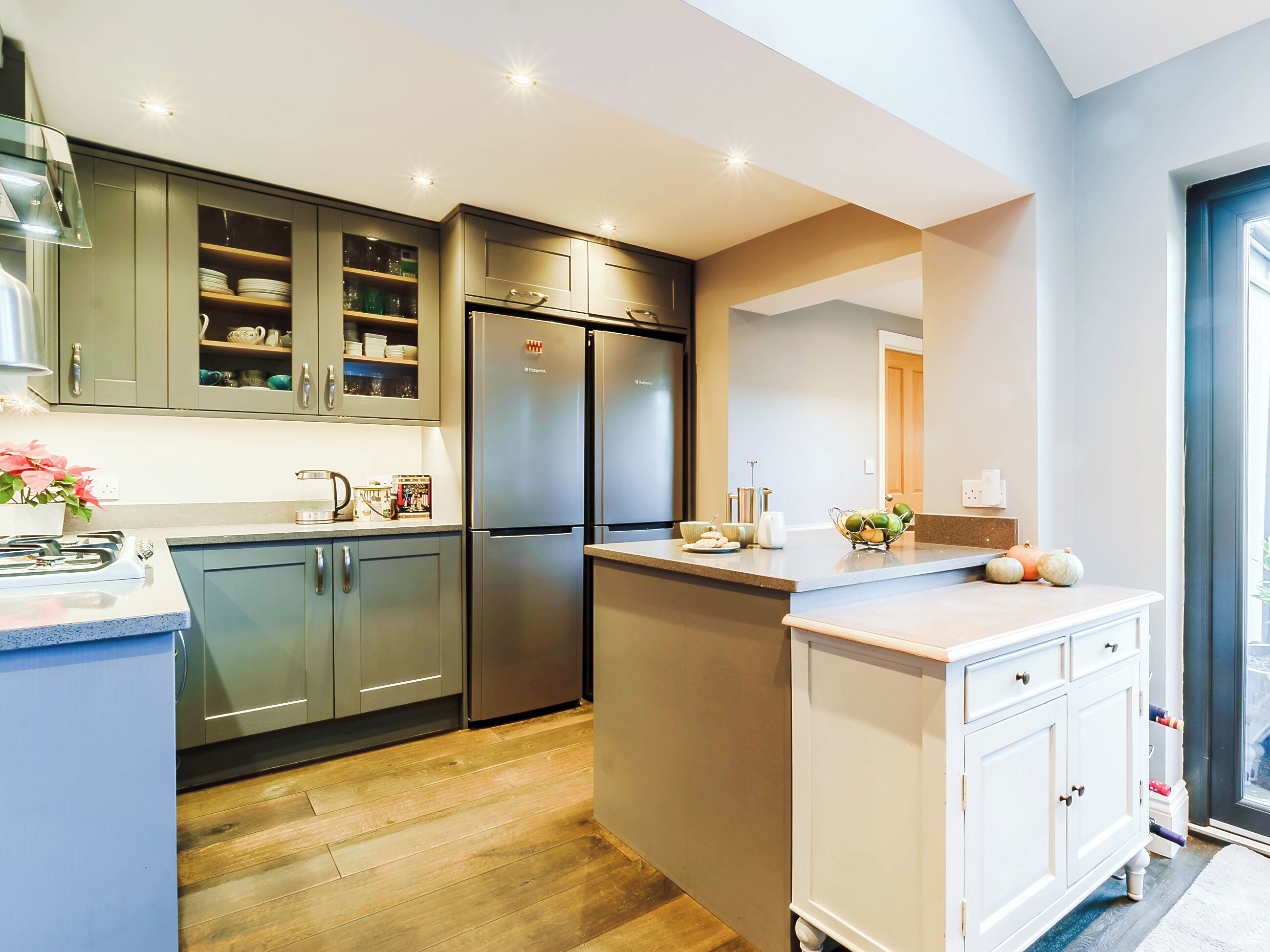 A modern kitchen with a built-in refrigerator, a stove, and a sink. There is a countertop with a bowl of fruit and a vase of flowers.