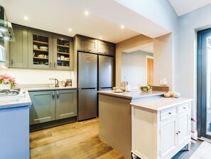Una cocina moderna con refrigerador empotrado, estufa y pileta. Hay una encimera con un cuenco de frutas y un jarrón de flores.