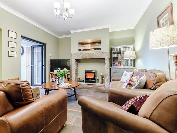 A spacious living room with leather sofas, a fireplace, a television, and a bookshelf.