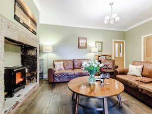 Una sala de estar acogedora con chimenea, sofás de cuero, una mesa de centro redonda de madera y una araña.
