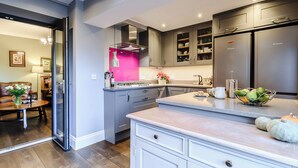 Une cuisine moderne avec des meubles gris, un réfrigérateur en acier inoxydable et un mur d’accent rose.