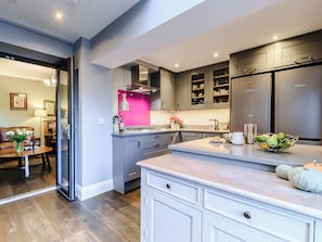 A modern kitchen with grey cabinets, a stainless steel refrigerator, and a pink accent wall.