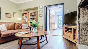 Un salon avec un canapé en cuir marron, une table basse en bois, une bibliothèque, un téléviseur et une porte donnant sur un balcon.