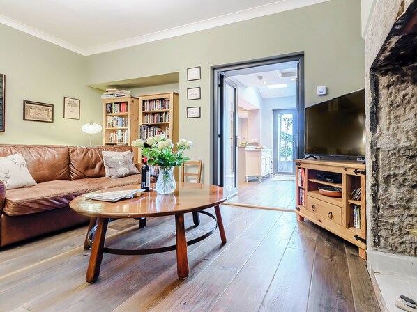 A living room with a brown leather sofa, a wooden coffee table, a bookshelf, a TV, and a door leading to a balcony.