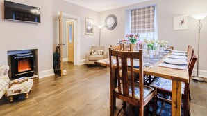 Un coin repas avec une table en bois dressée pour six personnes, une cheminée et un téléviseur fixé au mur.