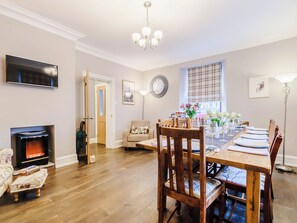 A dining area with a wooden table set for six, a fireplace, and a television mounted on the wall.