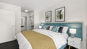 Une chambre d’hôtel moderne avec un lit soigneusement fait, une table de chevet avec une lampe et deux tableaux encadrés accrochés au mur.